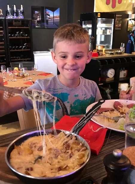 Enfant assis à table avec plat de pâtes.
